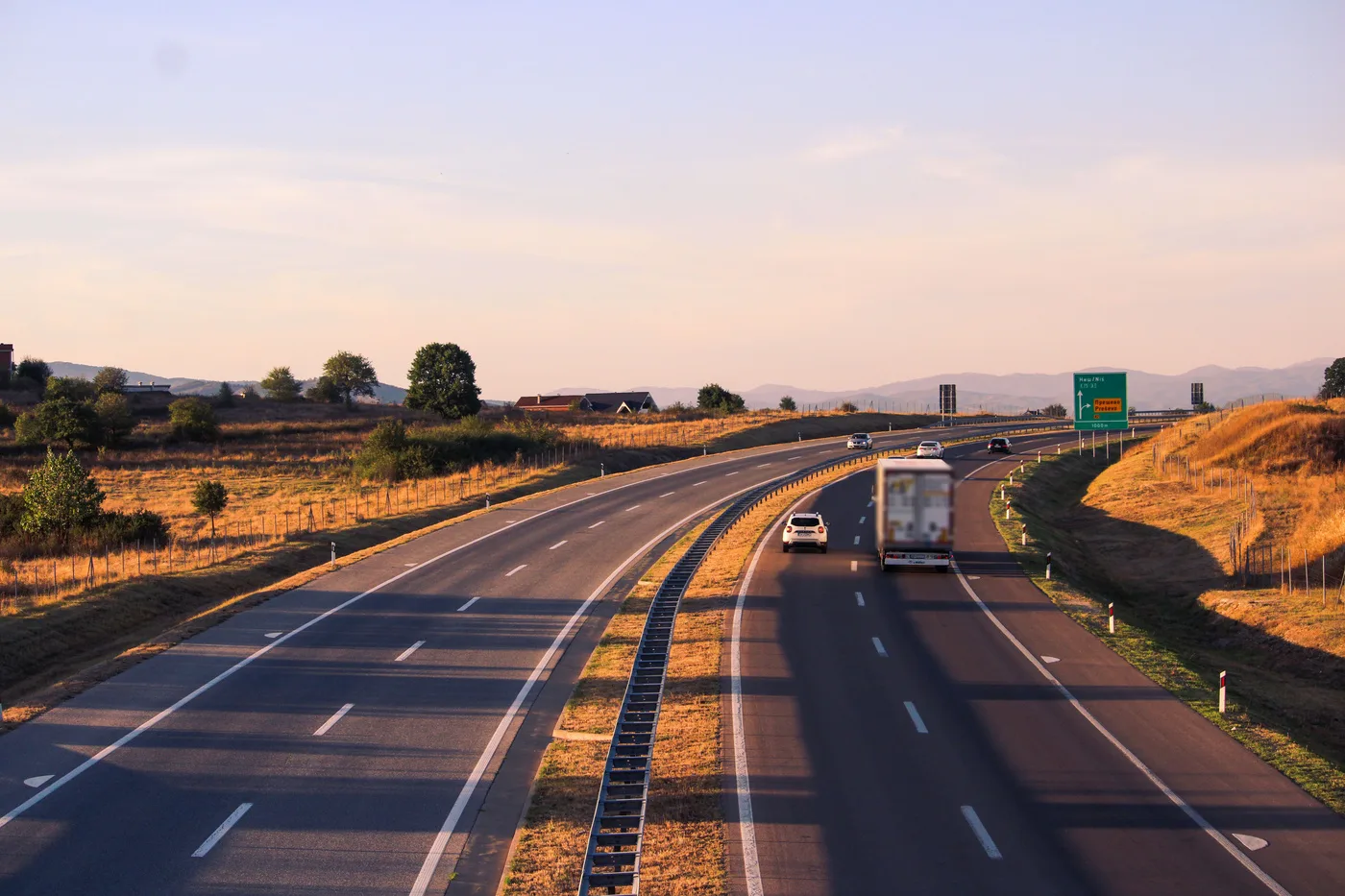 Ciężarówka i samochody osobowe na autostradzie wśród wzgórz w świetle zachodzącego słońca